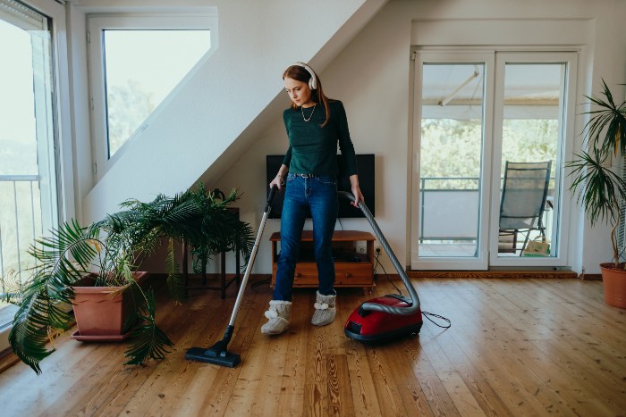 Woman vacuuming hardwood floor with headphones.