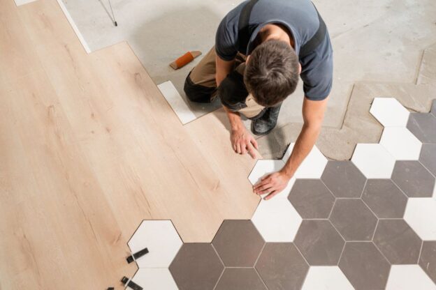Worker installing wood and hexagon tile floor.