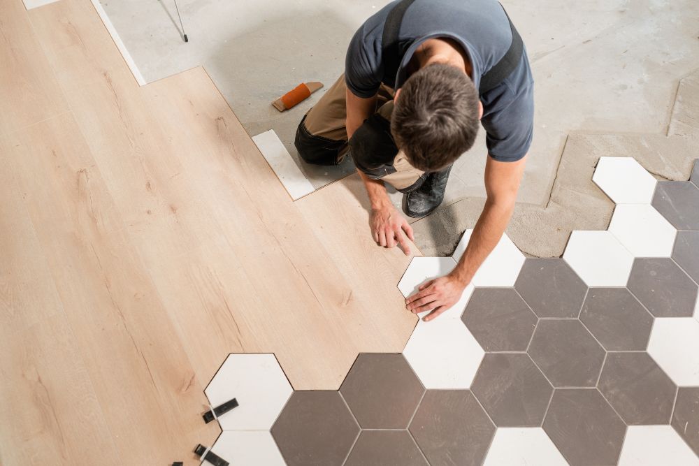 Worker installing wood and hexagon tile floor.