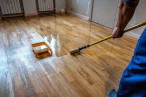 Here's a short alt tag for the image: `Person applying varnish to hardwood floor`